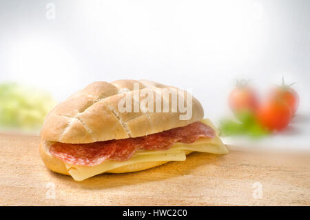 inviting sandwich with salami and cheese on wooden desk with blurred foggy tomatos and lettuce background Stock Photo