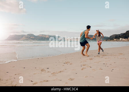 Shot of fit young couple playing on the beach. Young man and woman running and playing on the sea shore. Stock Photo