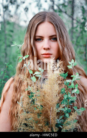 Portrait of spring girl in green trees,flowers,garden,park.Long-haired light-haired blonde girl,woman with bouquet of green flowers in hands.Springtim Stock Photo