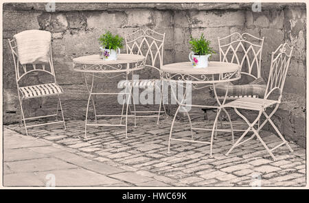 Cirencester - ornate wrought iron tables and chairs with plant pots in a corner of Cirencester, Gloucestershire in March Stock Photo