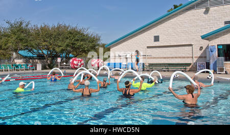 Group of women, 1 man, including seniors, attending Water Aerobics class, instructor demonstrating,  using  styrofoam 'water noodle'. Stock Photo