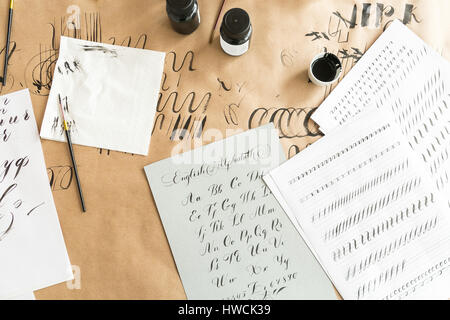 Calligraphy sheets, nibs, paper, ink and pens on a kraft background. Lettering calligraphy workshop. learning calligraphy - paper with example and brush and ink. Concept hobby. Stock Photo