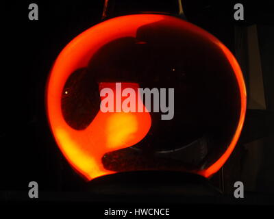 detail of large pharmacy jar with red light at night creating bright orange circle surrounding distorted glowing bulb with dark background Stock Photo