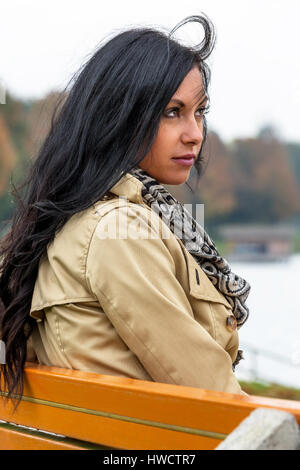 A young woman sits thoughtfully on a park-bench, Eine junge Frau sitzt nachdenklich auf einer Parkbank Stock Photo