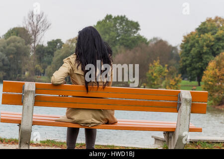 A young woman sits thoughtfully on a park-bench, Eine junge Frau sitzt nachdenklich auf einer Parkbank Stock Photo