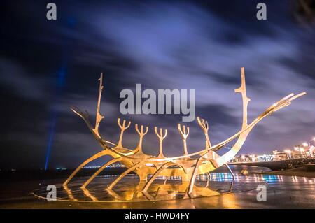 Iceland,Reykjavik,night view on Sólfar (The Sun Voyager),illuminated sculpture located in the old city harbor,conducted in 1990 by Jón Gunnar Árnason,made of steel,it evokes the silhouette of a Viking boat who goes to the setting sun,in the background the Imagine Peace tower (Friðarsúlan),on the island of Viðey,a monument inaugurated in Iceland in 2007 by Yoko Ono in memory of her husband John Lennon,tower of light projected from a white stone base,every day between 9 October and 8 December each year (anniversaries of the birth and death of the artist) Stock Photo