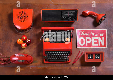 High Angle Still Life of Collection of Red Objects on Wood Desk - Speaker, Radio, Typewriter, Open Sign, Clock, Pencils, Telephone, Pool Balls and Mic Stock Photo