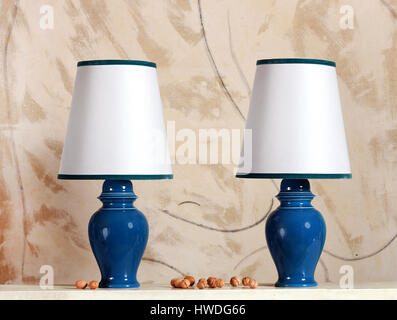 Pair of blue ceramic electric lamps with white shades trimmed in a matching blue standing on a table with whole fresh walnuts Stock Photo