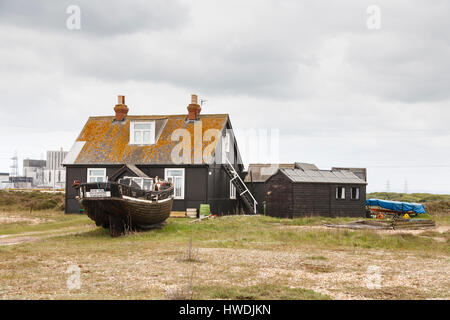 House on the shingle beach at Dungeness, Shepway district, Kent with an old wooden fishing boat in the garden and the nuclear power station behind Stock Photo
