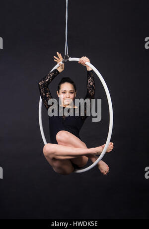 Aerial acrobat in the ring. A young woman performs the acrobatic elements in the air ring. Studio shooting performances on a black background. Stock Photo