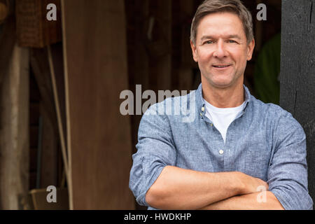 Portrait shot of an attractive, successful and happy middle aged man male arms folded outside wearing a blue shirt outside his garage or shed Stock Photo