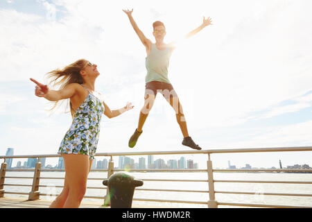 Young man jumping mid air on sunlit waterfront, New York, USA Stock Photo