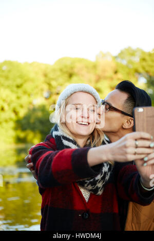 Couple taking smartphone selfie by park lakeside Stock Photo