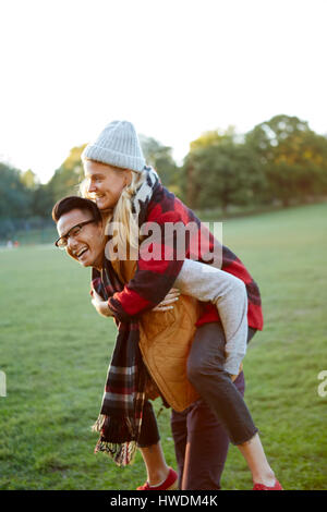 Man giving girlfriend a piggyback in park