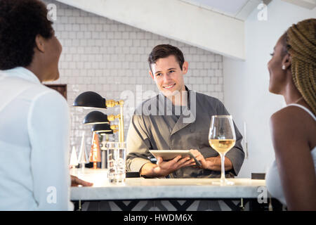 Barman serving customers at bar, barman using digital tablet Stock Photo