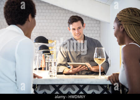 Barman serving customers at bar, barman using digital tablet Stock Photo