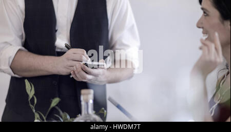 Waiter serving diner in restaurant, using pen and notepad, mid section Stock Photo
