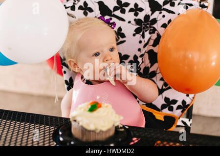 Baby girl sitting in high chair, eating birthday cake Stock Photo
