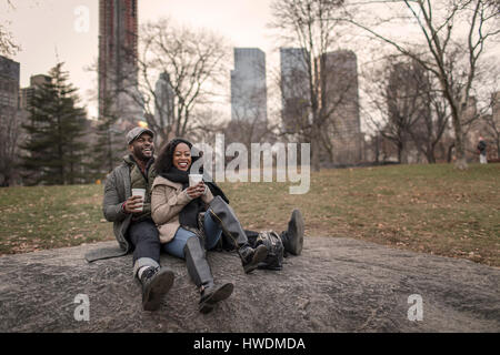 Couple sitting on rock in park with takeaway coffee Stock Photo