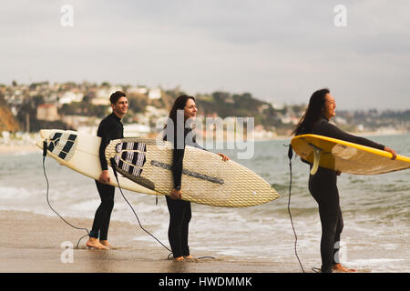 Three friends standing in sea, holding surfboards, preparing to surf Stock Photo