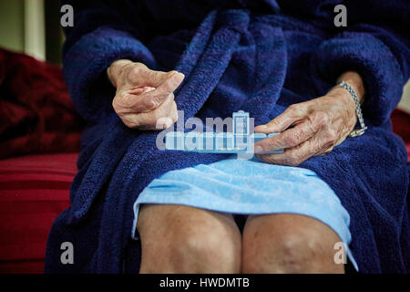 Senior woman sitting on edge of bed, taking tablets from pill organiser, mid section Stock Photo