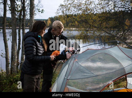 Young Couple Setting Up Tent By Lake Stock Photo