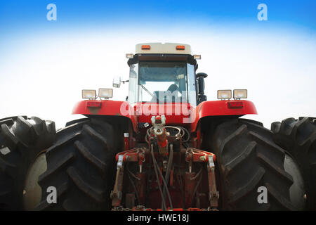 Modern red tractor on a blue sky background close-up. Stock Photo