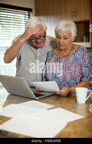 Senior couple calculating their invoices with laptop in the kitchen at home Stock Photo