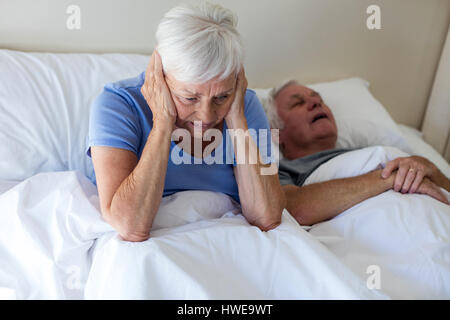 Senior woman getting disturbed with man snoring on bed in bedroom Stock Photo