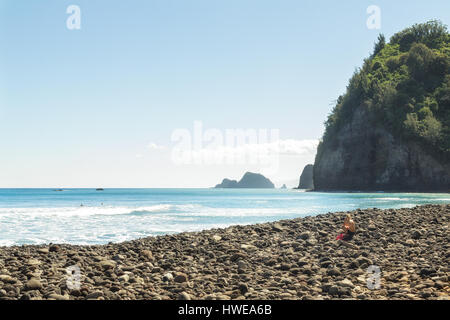 People enjoy the rocky beach after hiking into the Pololu Valley at the north end of the Big Island of Hawaii. Unrecognizable woman sitting on rock an Stock Photo