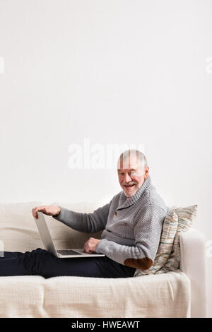 Senior man sitting on sofa, working on laptop. Stock Photo