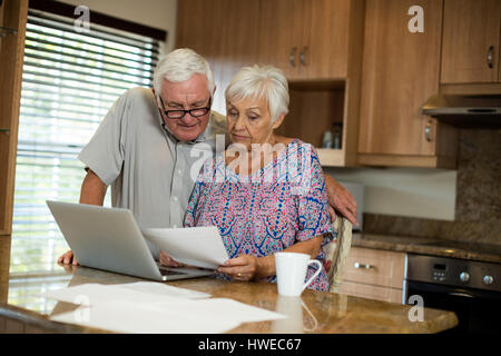 Senior couple calculating their invoices with laptop in the kitchen at home Stock Photo