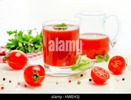 tomato juice in glass, jug with greenery, basil, cutted tomato fruit and dry pepper on light table, concept vegetarian food, close up Stock Photo