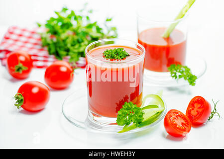 tomato juice in transparent glasses with parsley, cutted tomato fruit, cucumber and red napkin, close up Stock Photo