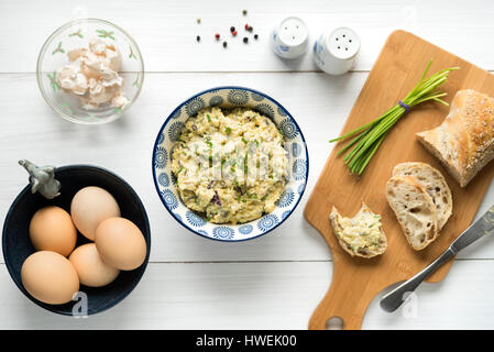 Homemade egg salad spread with mayonnaise, mustard, red onion sprinkled with chives, top view background on white table. Stock Photo