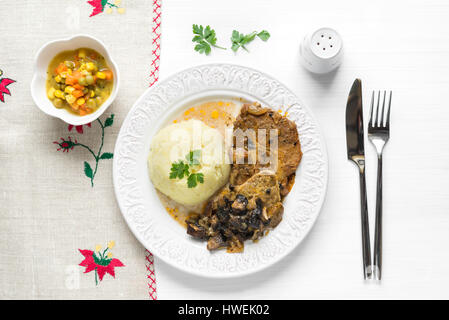 Top view of cooked pork chop steak with mushroom sauce, mashed potatoes and boiled carrot salad on white table Stock Photo