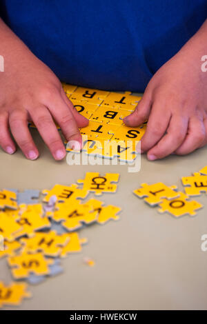 Hands of preschool boy doing jigsaw alphabet in classroom Stock Photo