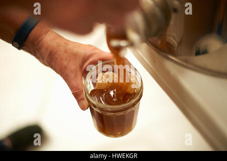 Hands of female beekeeper pouring honey into jar from kitchen vat Stock Photo