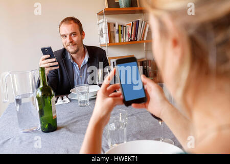 Mid adult couple at home, sitting at dinner table, using smartphones Stock Photo