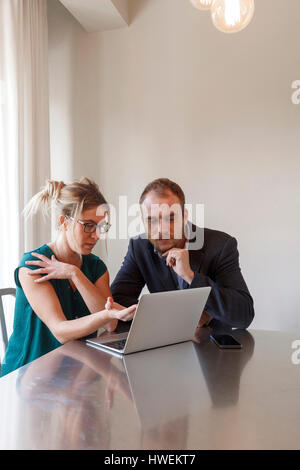 Mid adult couple sitting at table, looking at laptop Stock Photo