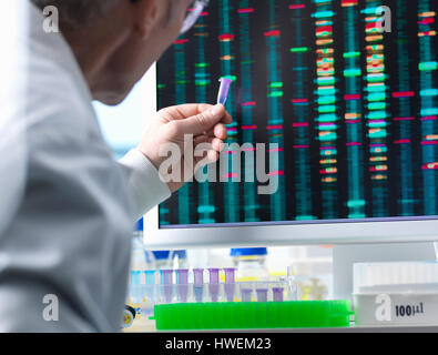 DNA Research, Scientist holding up a DNA sample with results on the computer screen Stock Photo