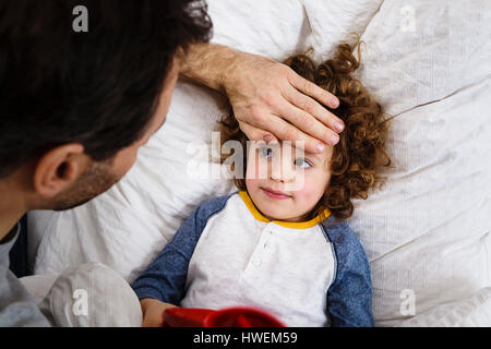 Overhead view of girl lying in bed with father's hand on forehead Stock Photo