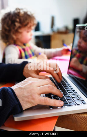 Close up of man's hands typing on laptop and daughter drawing at table Stock Photo