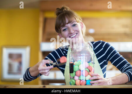Portrait of young woman in food shop, taking sweet food from jar Stock Photo