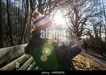 Mother sitting on bench with baby boy, taking selfie with smartphone Stock Photo