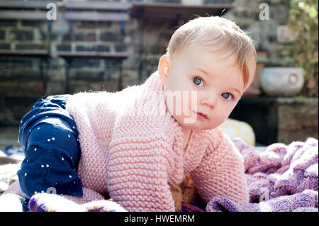 Portrait of baby girl crawling on knitted blanket in garden Stock Photo