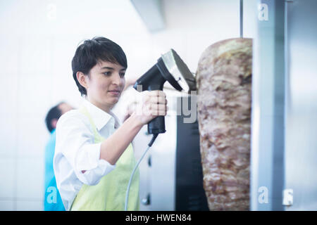 Young woman slicing kebab meat in fast food shop Stock Photo