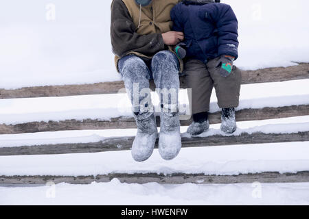 Father and son sitting on fence on snow covered landscape Stock Photo