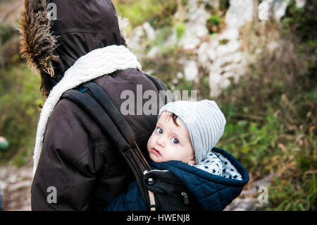Portrait of baby boy wearing knit hat, carried in baby sling by mother Stock Photo