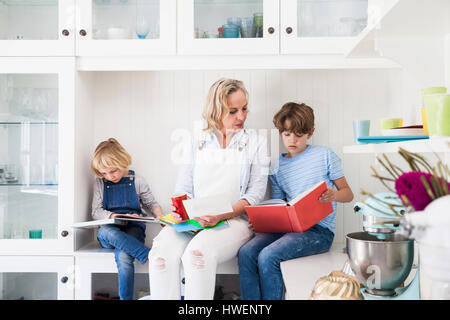 Mature woman sitting on kitchen counter reading storybooks with son and daughter Stock Photo